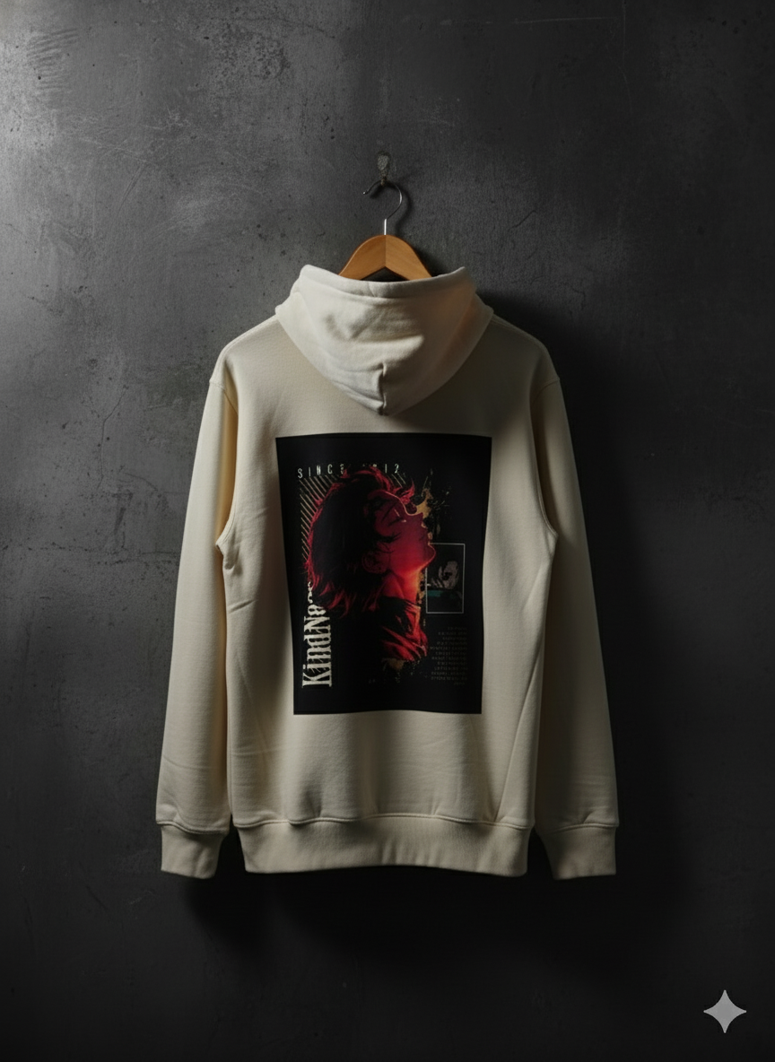 Beige hoodie with a graphic design on the back, hanging against a dark gray wall.